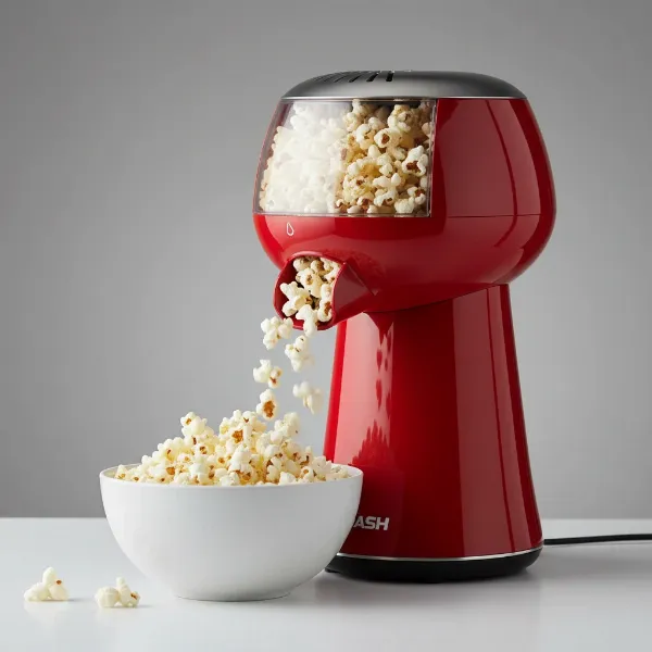 A vibrant red DASH Hot Air Popcorn Maker popping popcorn into a large white bowl for healthy snacking.